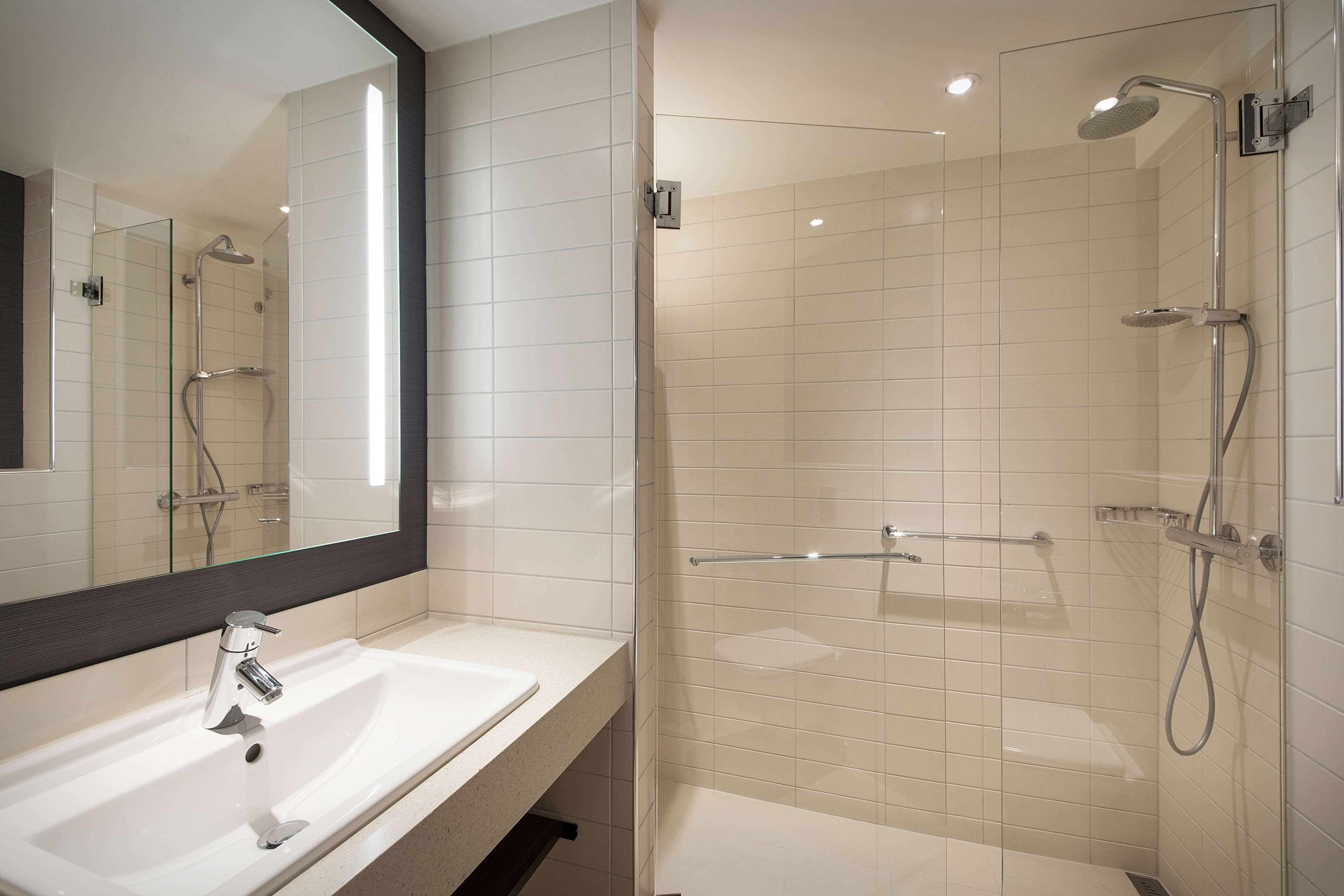 Un baño moderno con lavamanos blanco, un espejo grande y una zona de ducha con mampara de vidrio.