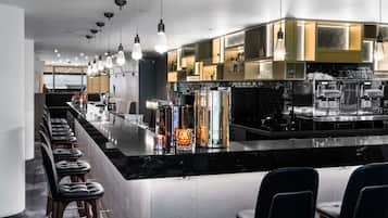 A modern bar area with a long counter, bar stools, and a variety of bottles and glasses.