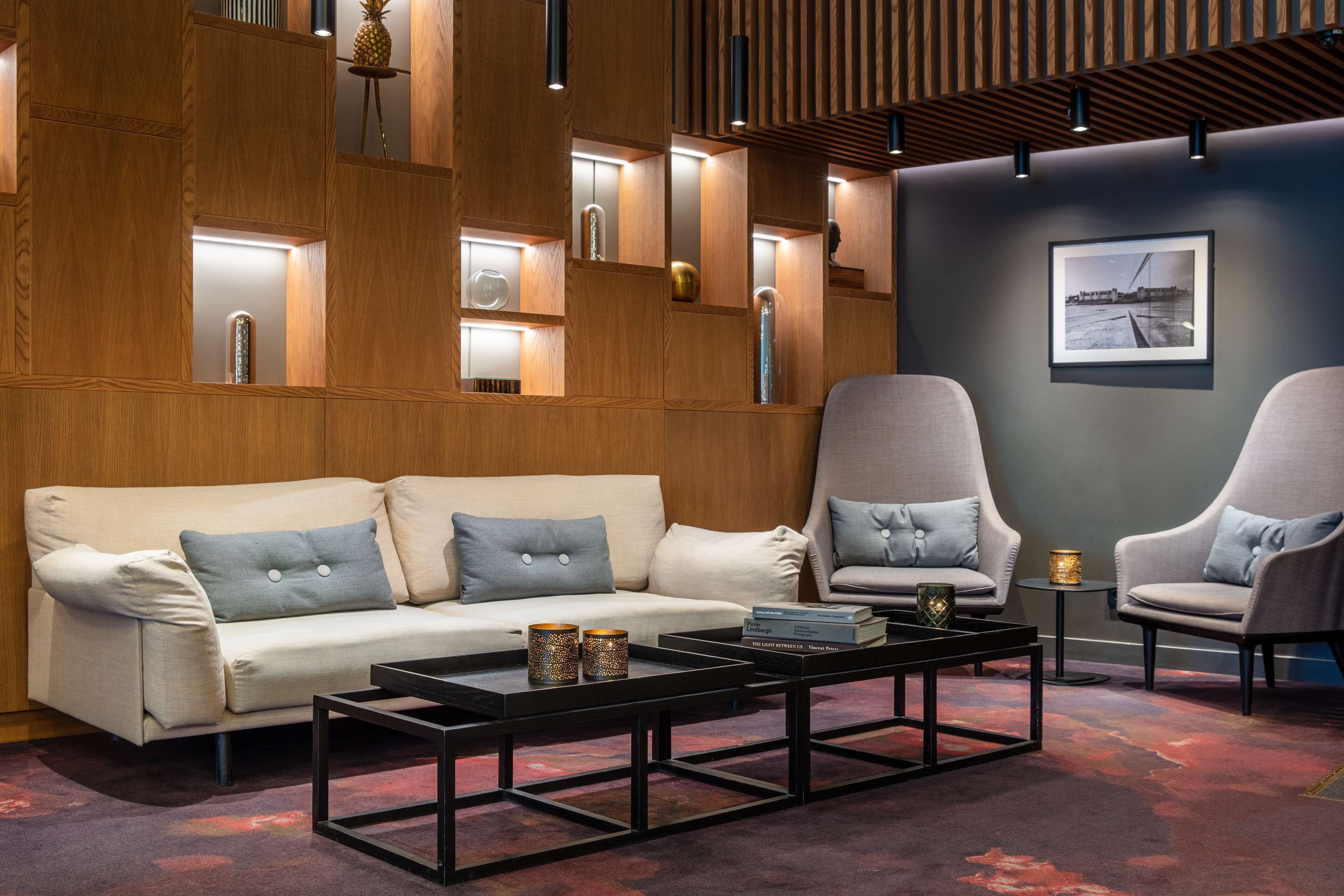 Un área de estar moderna con un sofá, sillones, una mesa de centro y un cuadro en la pared.