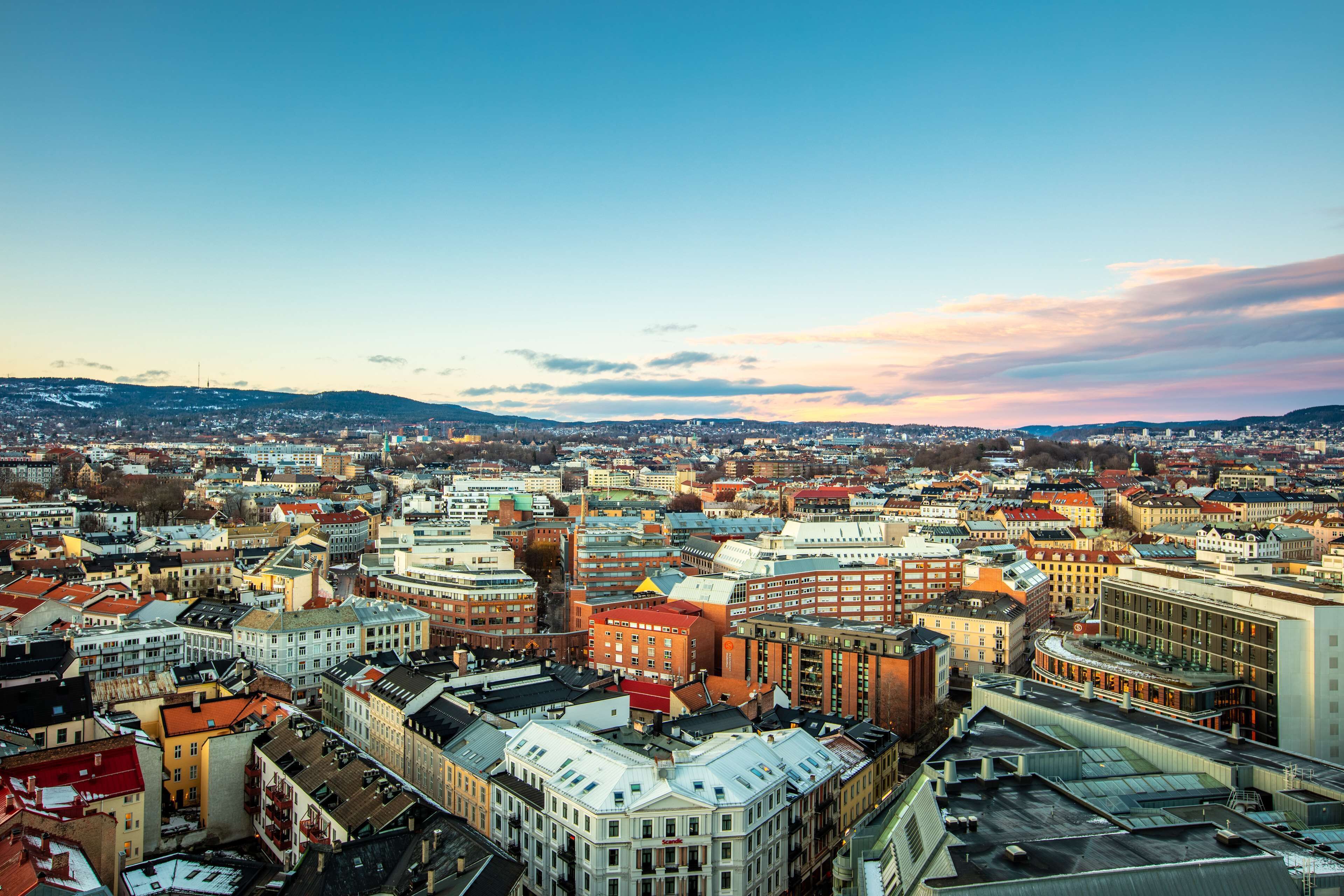 Vista panorámica de un paisaje urbano con una mezcla de edificios históricos y modernos, cielo despejado y montañas al fondo.