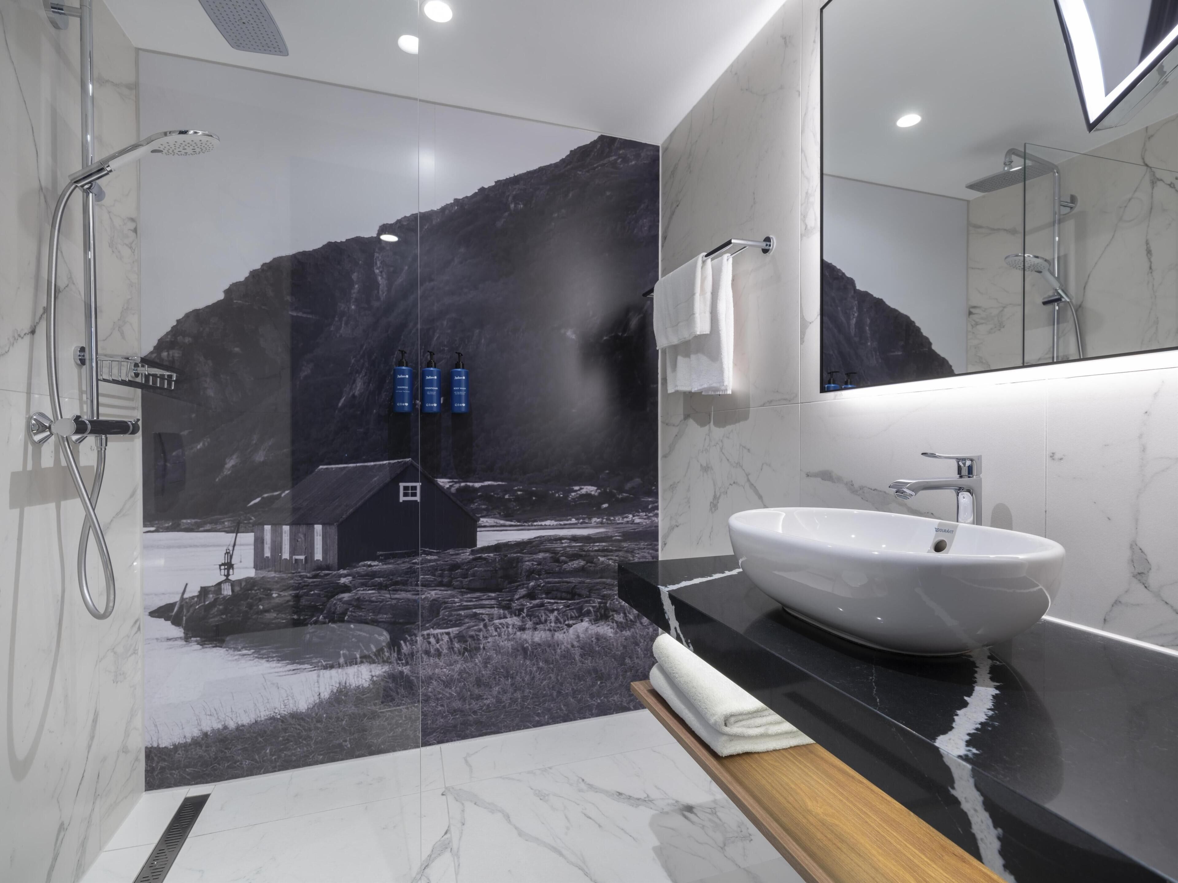 A modern bathroom with a large mirror, a white sink, and a shower.