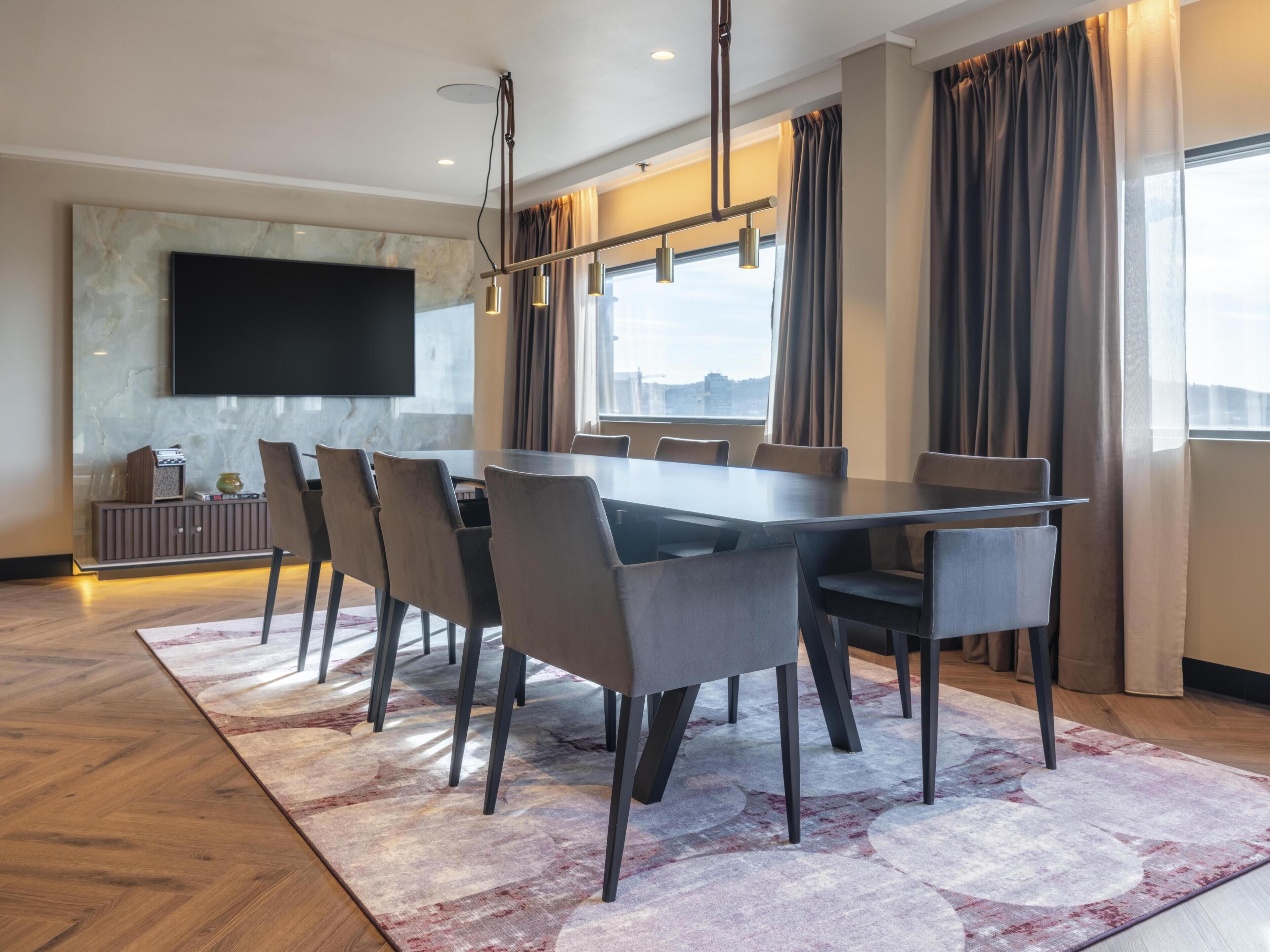A modern dining area with a large table, chairs, a flat-screen TV, and a city view.