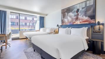 Habitación de hotel con una cama grande, un escritorio y una silla. Se ve una ventana con vistas a un edificio y un balcón.