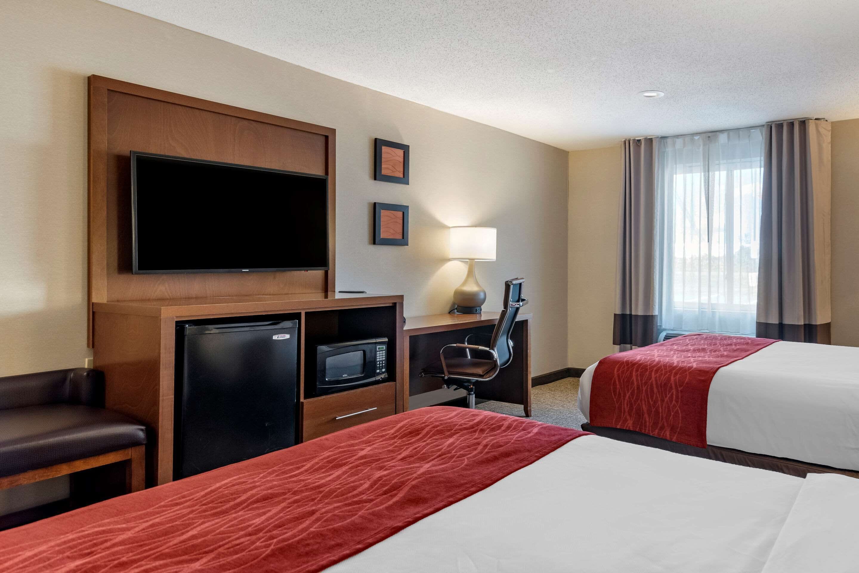 A hotel room with two beds, a TV, a desk with a computer, a microwave, and a chair.