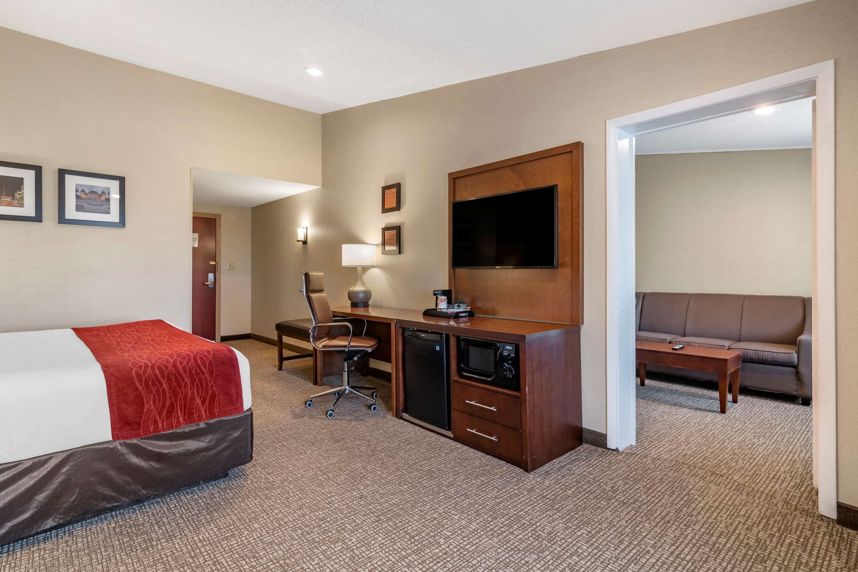 A hotel room with a bed, desk, chair, microwave, and a TV.