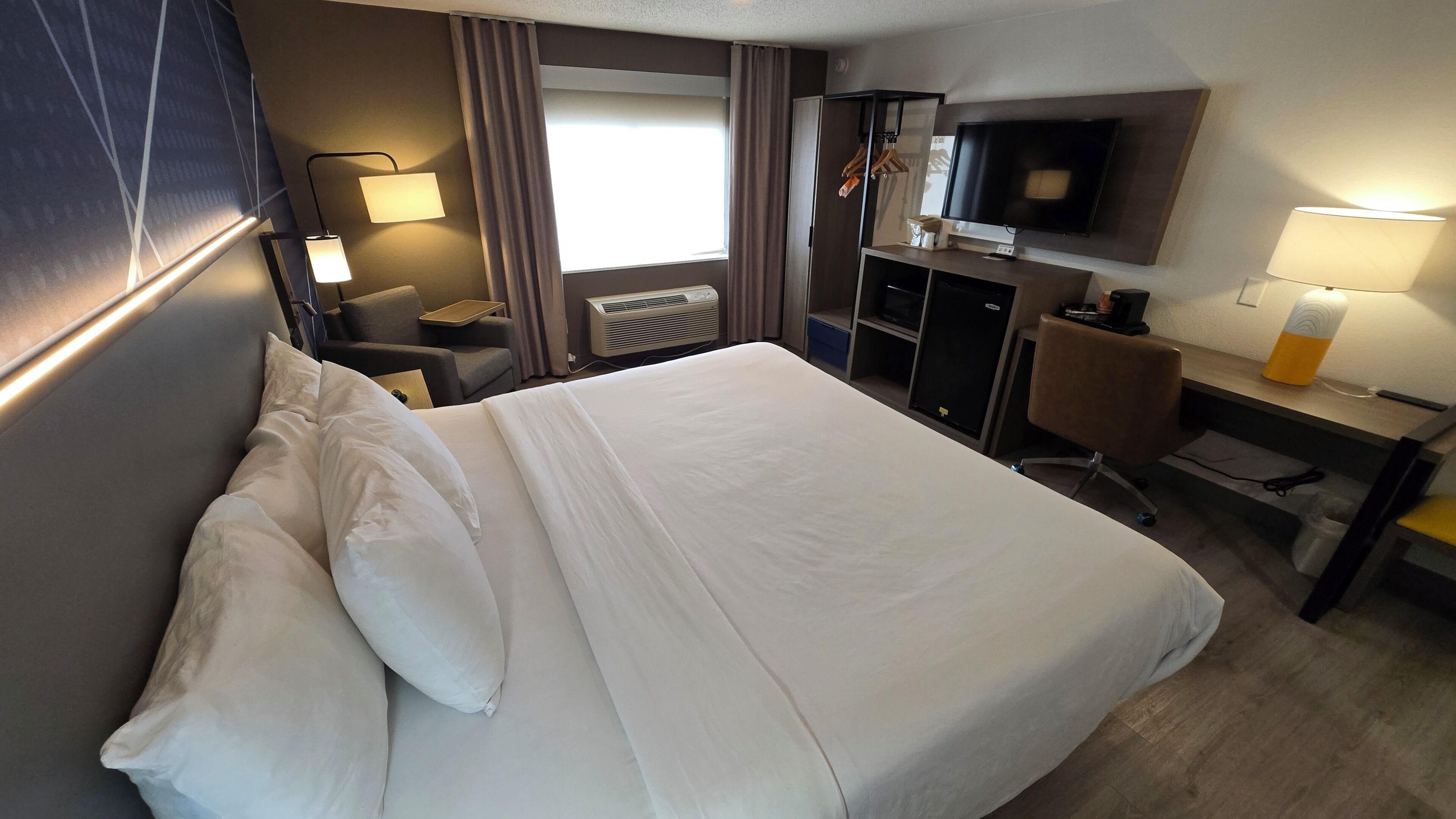 A hotel room with a bed, desk, chair, TV, and a window with curtains.