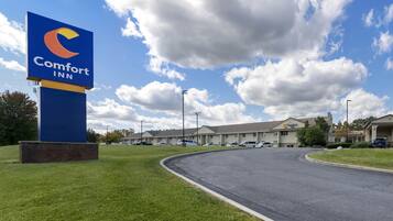 A Comfort Inn sign with a large blue and orange logo, a parking lot, and a row of hotel buildings under a partly cloudy sky.