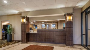 A reception area with a wooden reception desk, a clock, and a potted plant. - Comfort Inn Glenmont - Albany South (Glenmont)