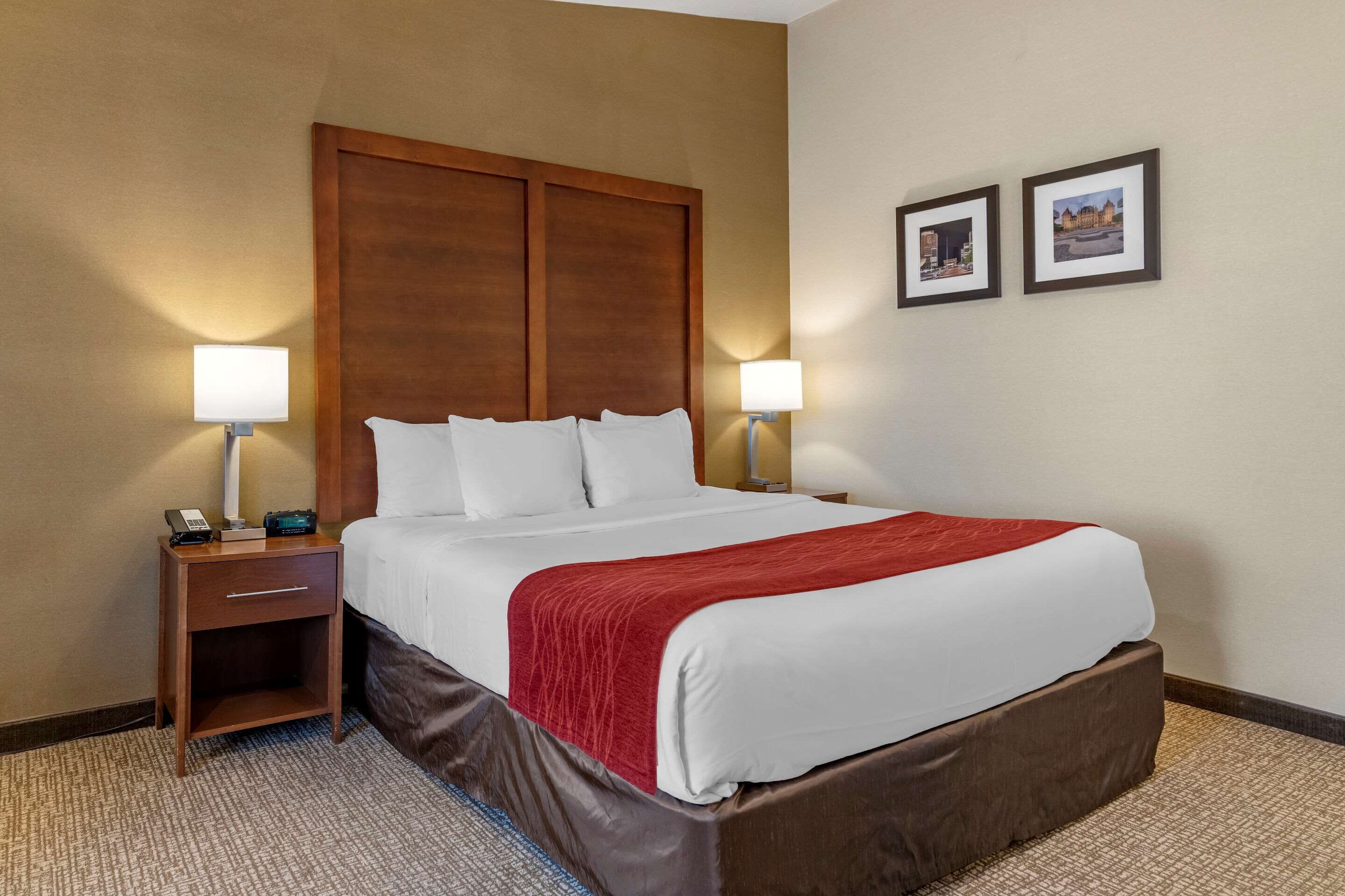 A hotel room with a large bed, two bedside lamps, a nightstand, and two framed pictures on the wall.