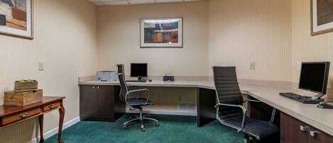 A conference room with a long table, two chairs, a desk with a computer, and framed artwork on the walls.