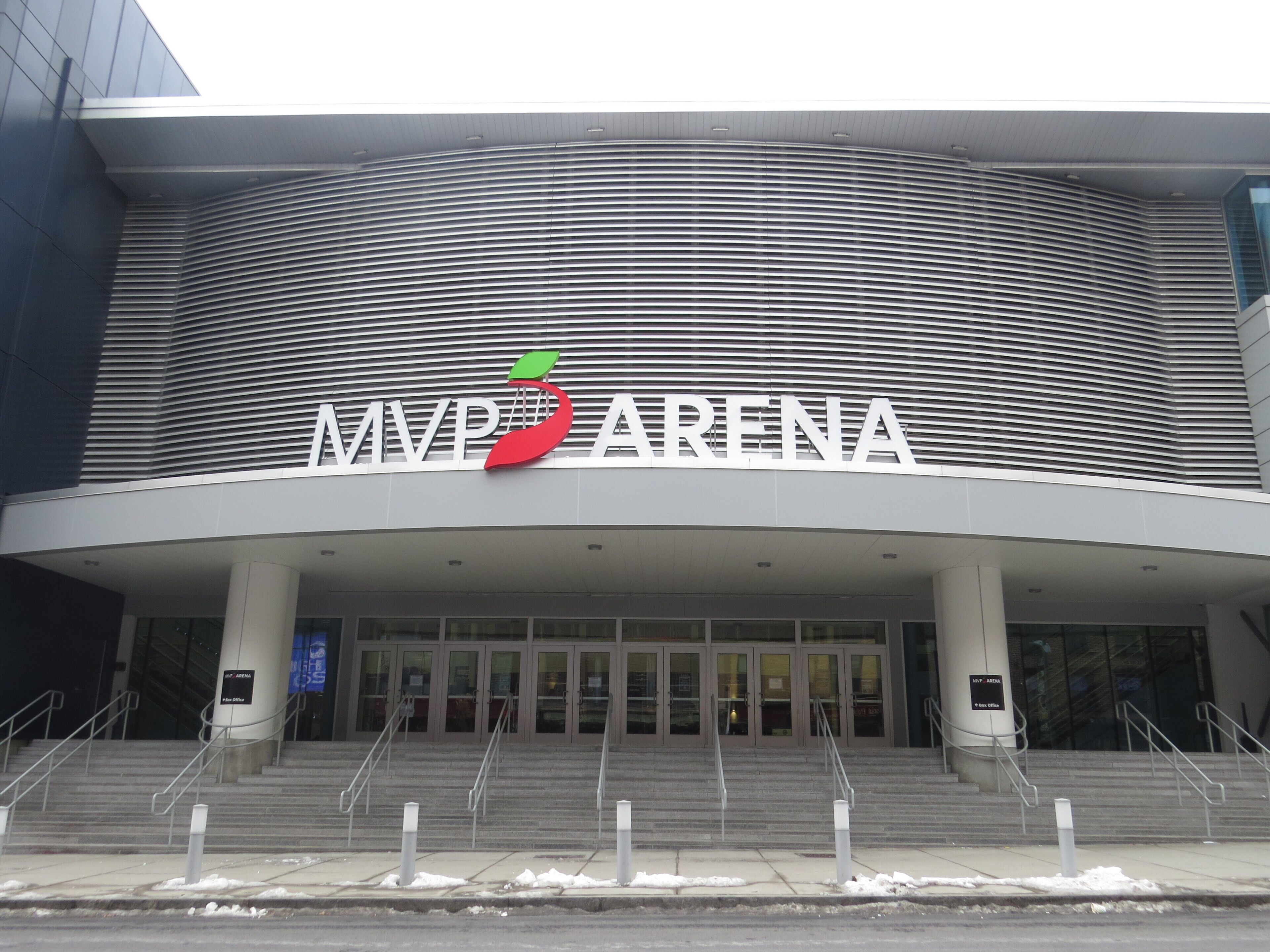 The exterior of the MVP Arena with a modern architectural design, featuring a curved facade and a prominent entrance with steps leading up to the doors.