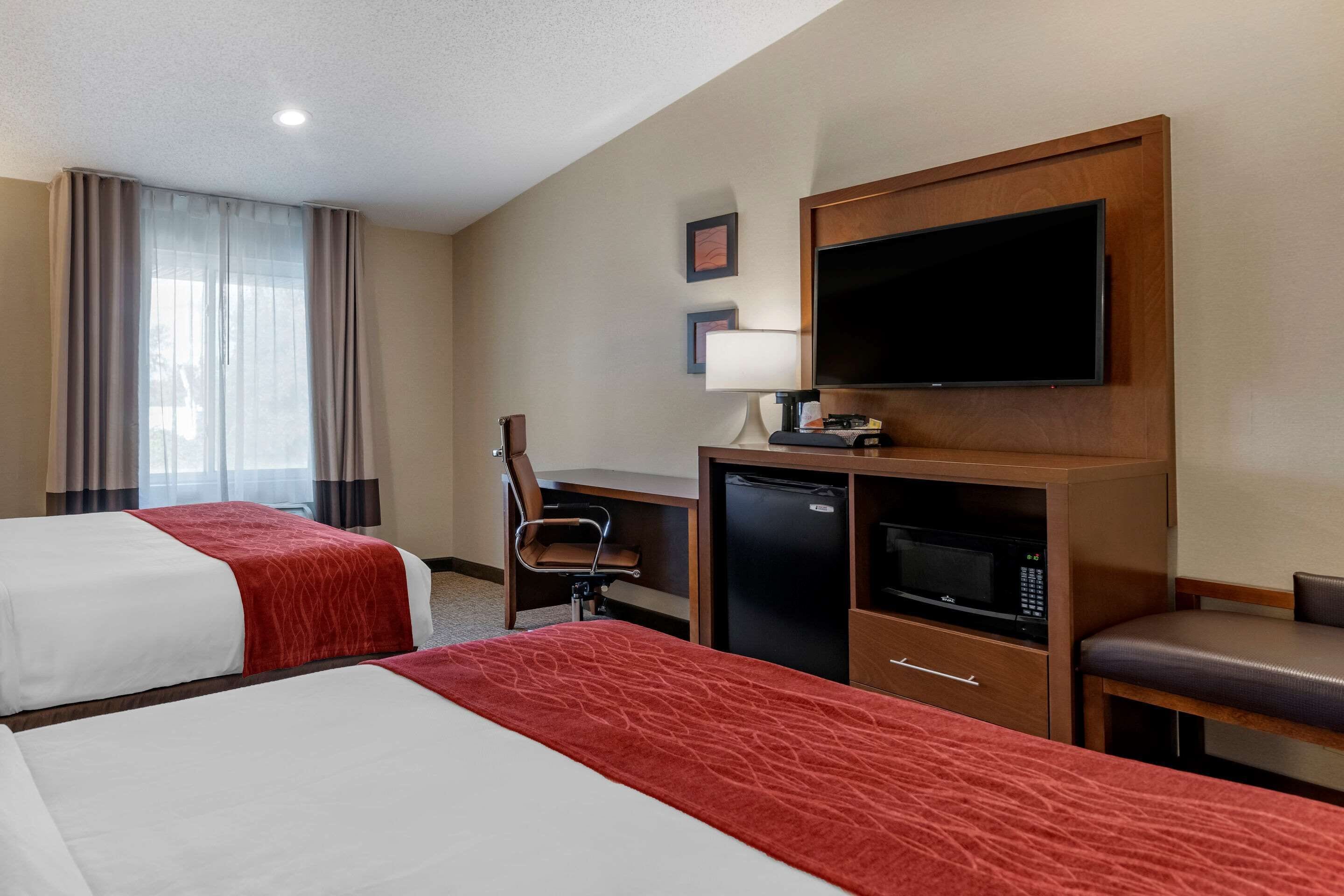 Habitación de hotel con dos camas, un escritorio con silla, televisor, microondas y un refrigerador pequeño.