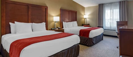 A hotel room with two beds, each with a red and white bedspread, wooden headboards, and a carpeted floor.