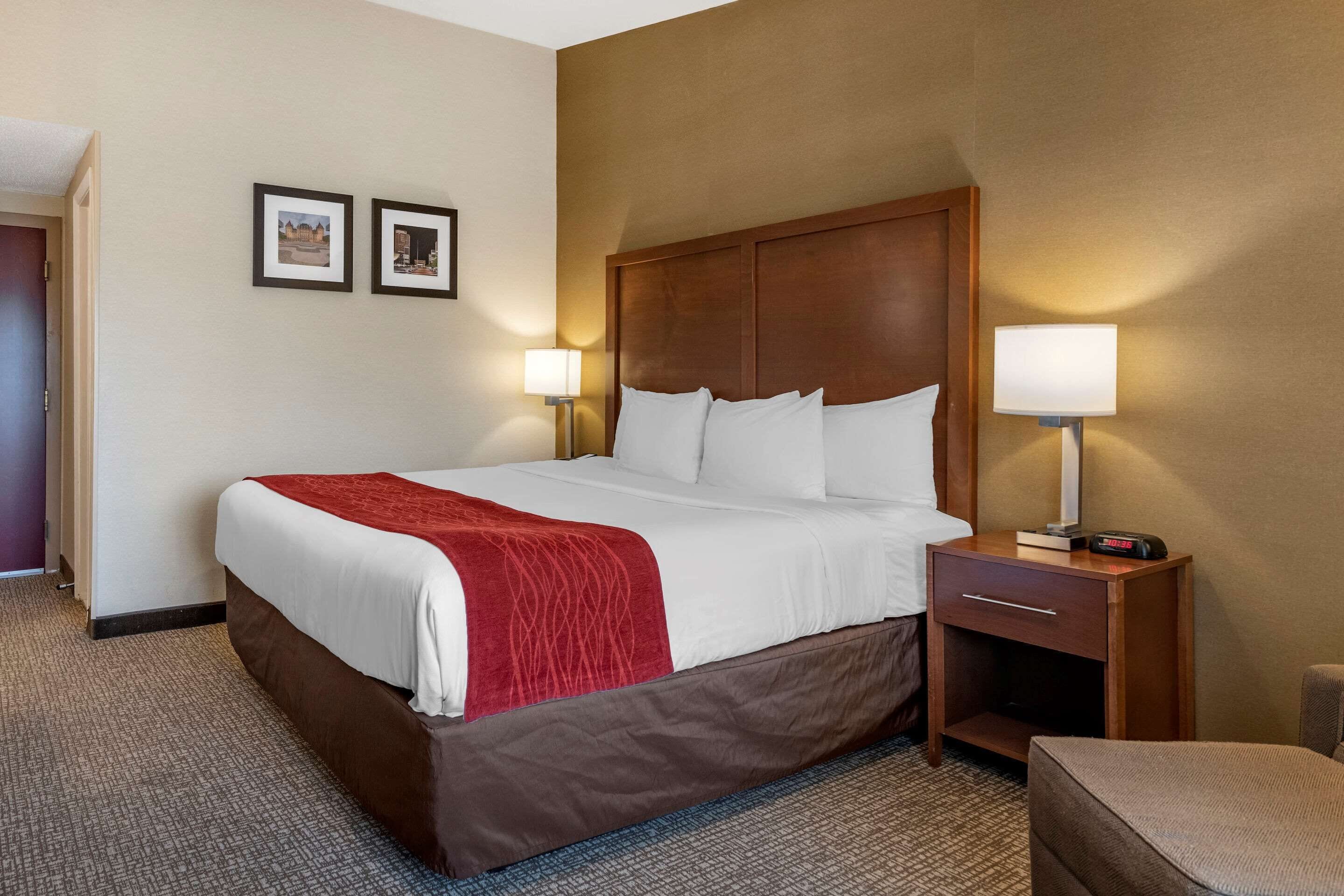 A hotel room with a large bed, two bedside lamps, a nightstand, and a chair.