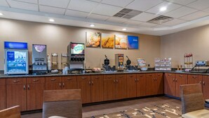A hotel kitchen with a coffee machine, a food display, and a seating area with a patterned rug. - Comfort Inn Glenmont - Albany South (Glenmont)