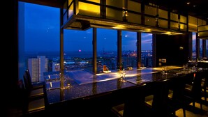 Un bar en un rascacielos con vistas panorámicas de la ciudad, amplias ventanas y una decoración interior moderna.