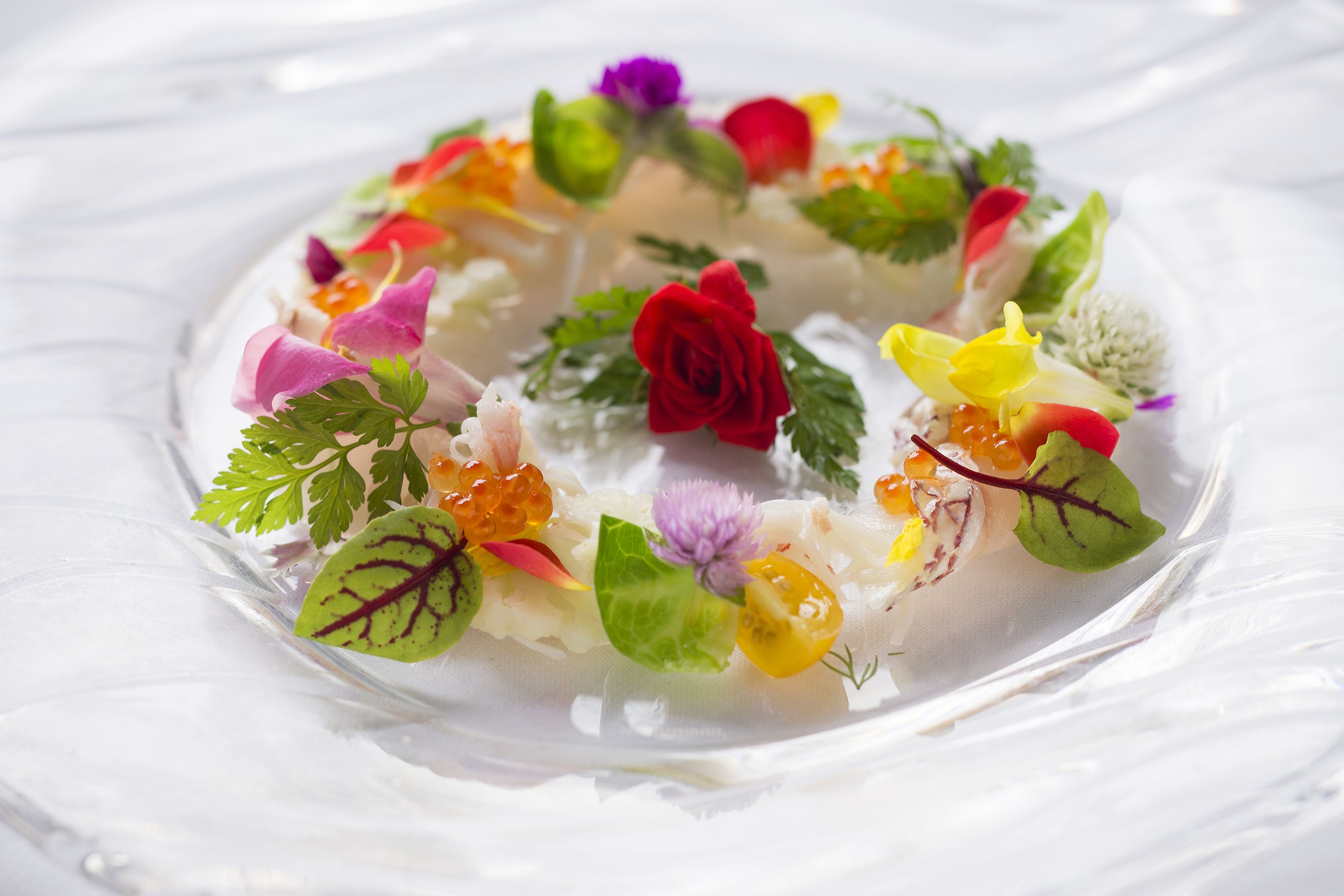 A glass dish with a variety of colorful flowers and leaves arranged in a circular pattern.