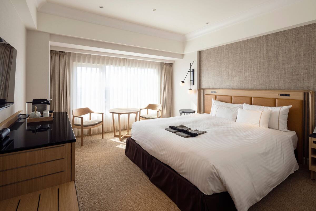 Habitación de hotel con una cama grande, un escritorio con una silla, una mesita y un televisor.