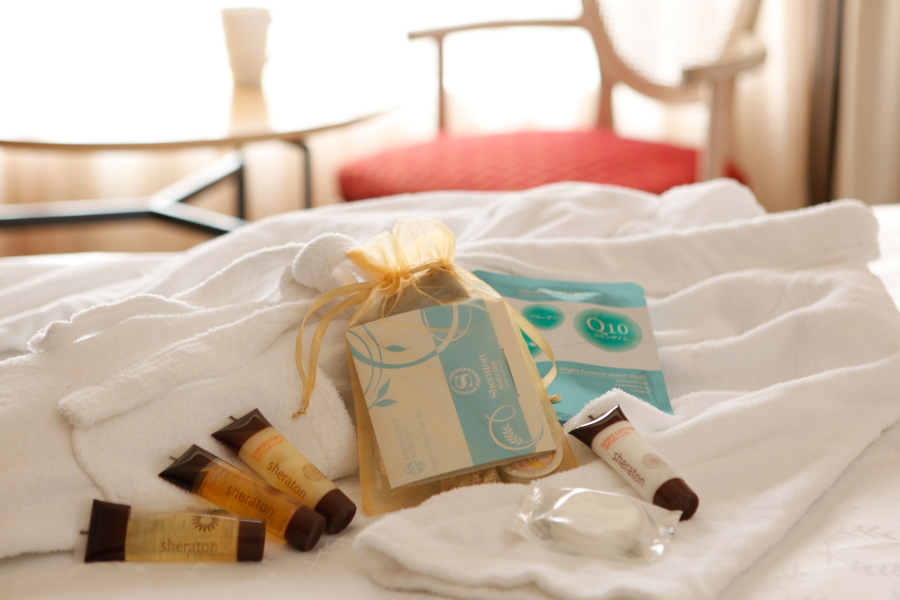 Una cama con una toalla blanca, una bolsa de regalo y artículos de aseo.