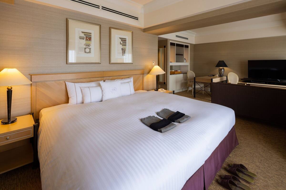 Habitación de hotel con una cama grande, dos lámparas de noche, un escritorio con una silla, televisión y cuadros en la pared.