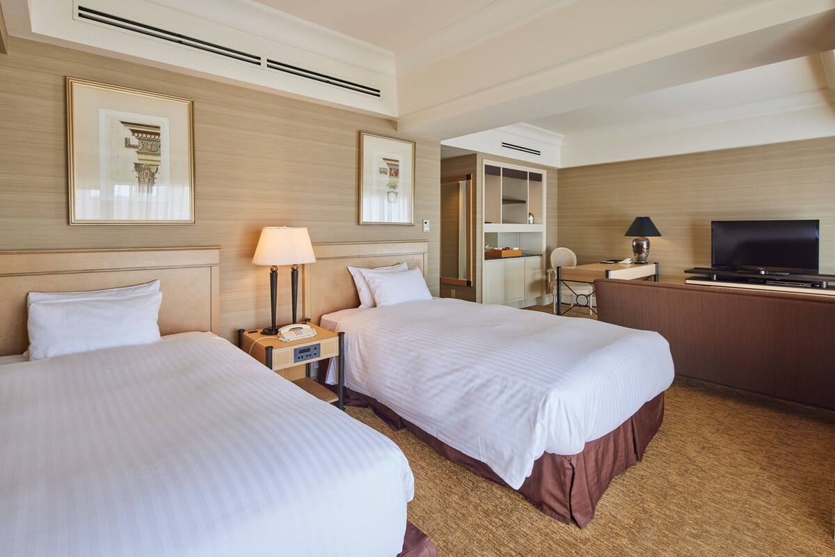 Una habitación de hotel con dos camas, un escritorio con televisor y un armario.