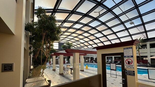 A pool area with a glass ceiling, poolside chairs, and a sign indicating no glassware allowed.