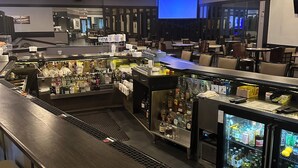 A bar area with a counter, stools, and refrigerators stocked with beverages.