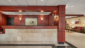 A reception area with a marble counter, a large abstract art piece, and a seating area with a sofa and lamps.