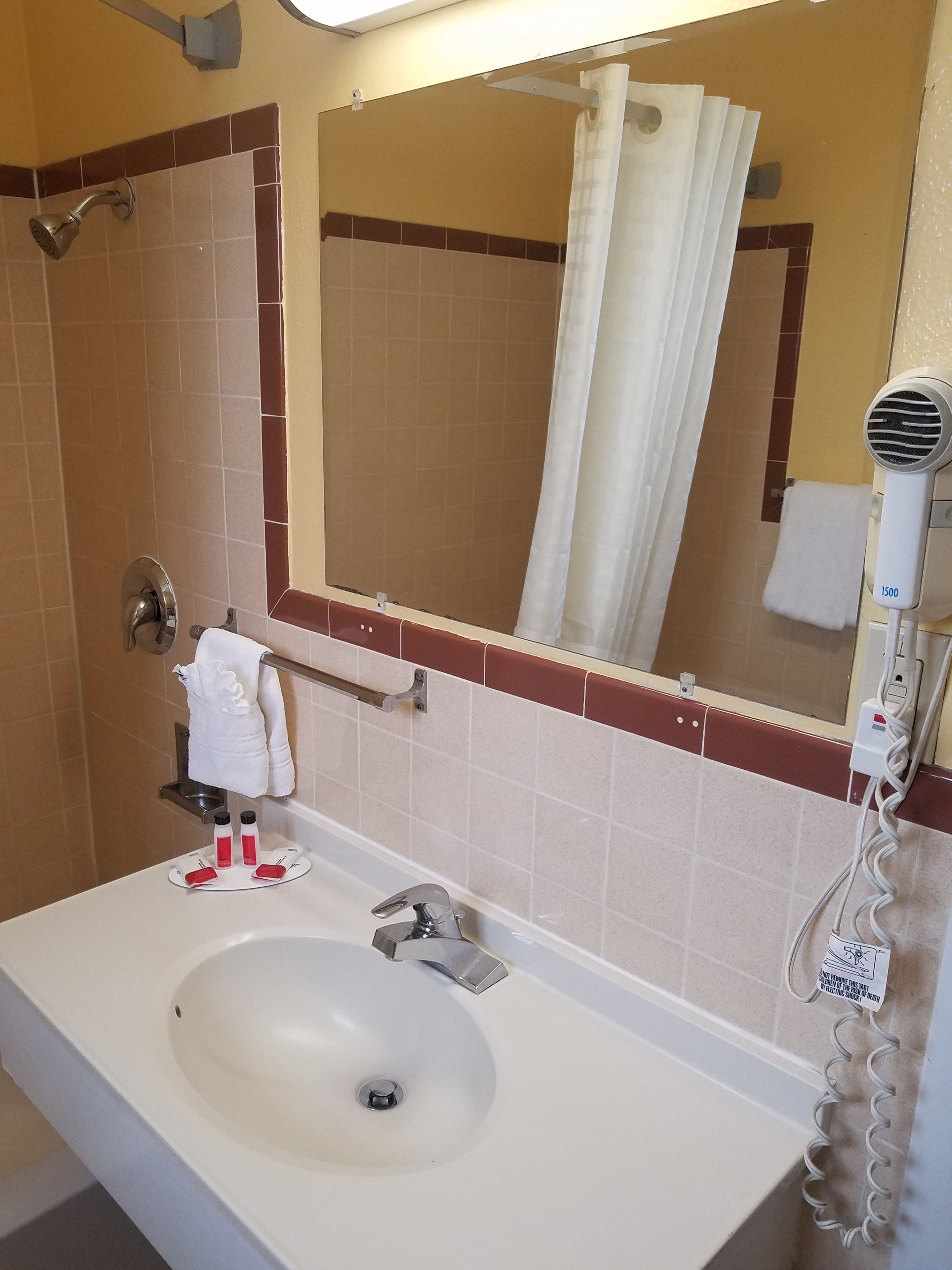 Een badkamer met een wastafel, spiegel, douche en haardroger.