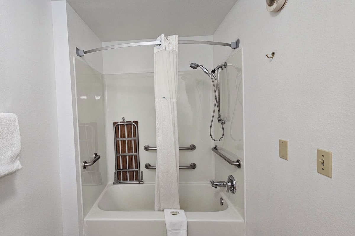 A shower with a glass door, a towel rack, a handrail, and a showerhead.
