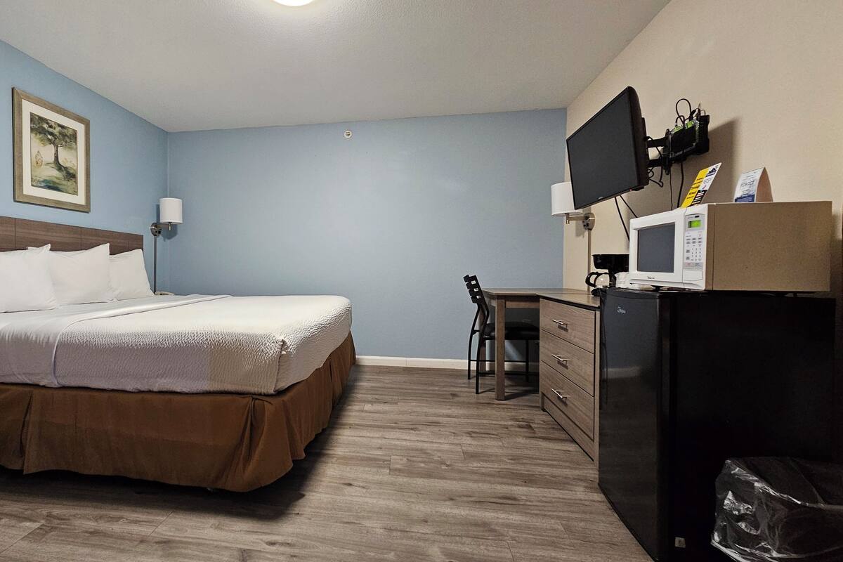 A hotel room with a bed, a desk, a chair, a television, and a refrigerator.