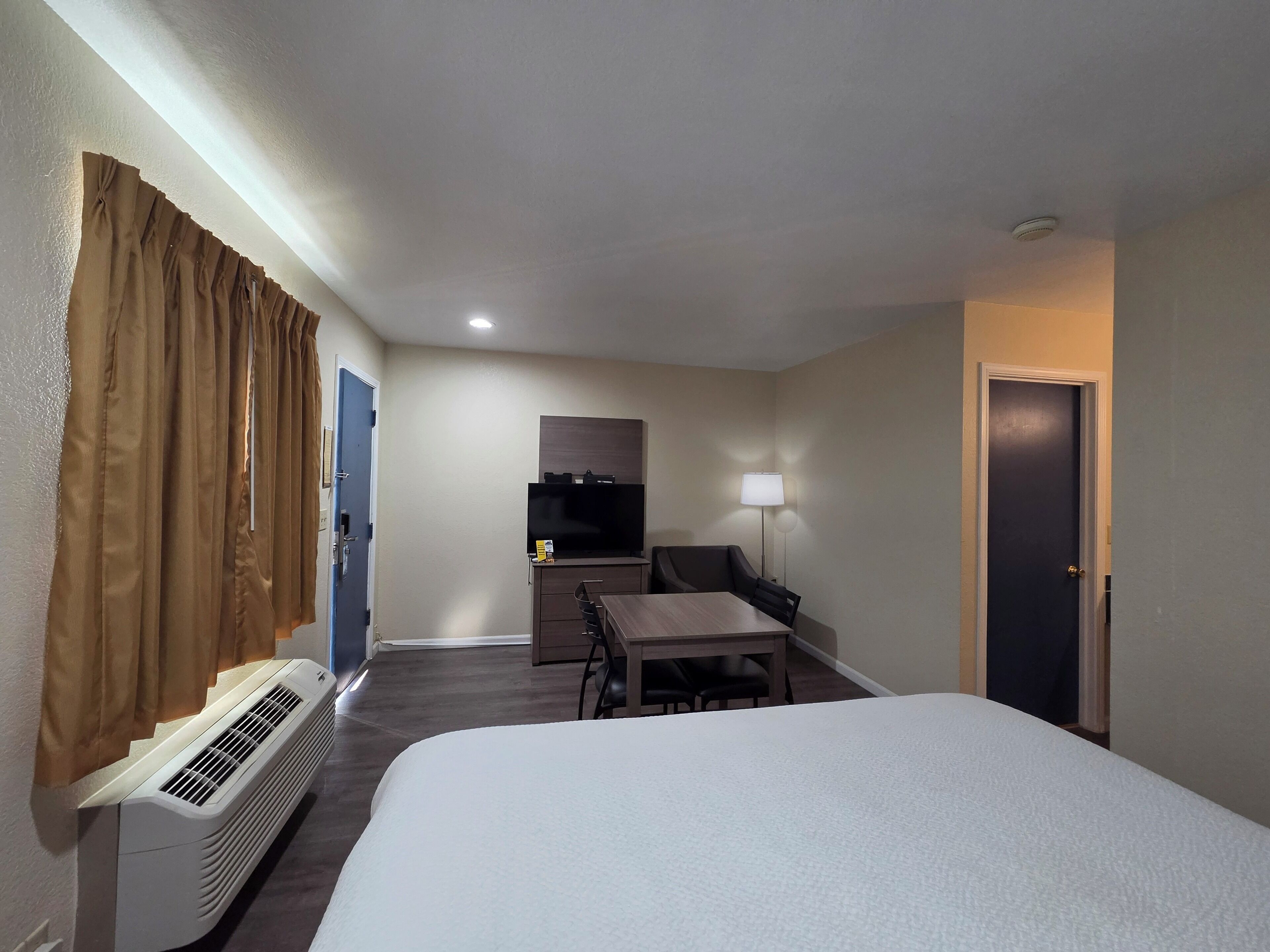 A hotel room with a bed, a desk, a chair, a television, a lamp, and a door.