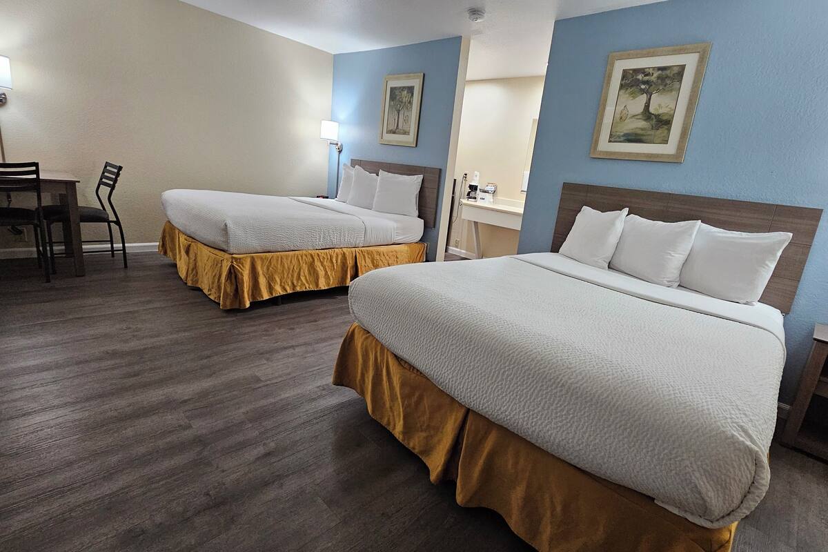 A hotel room with two beds, a desk, and chairs.