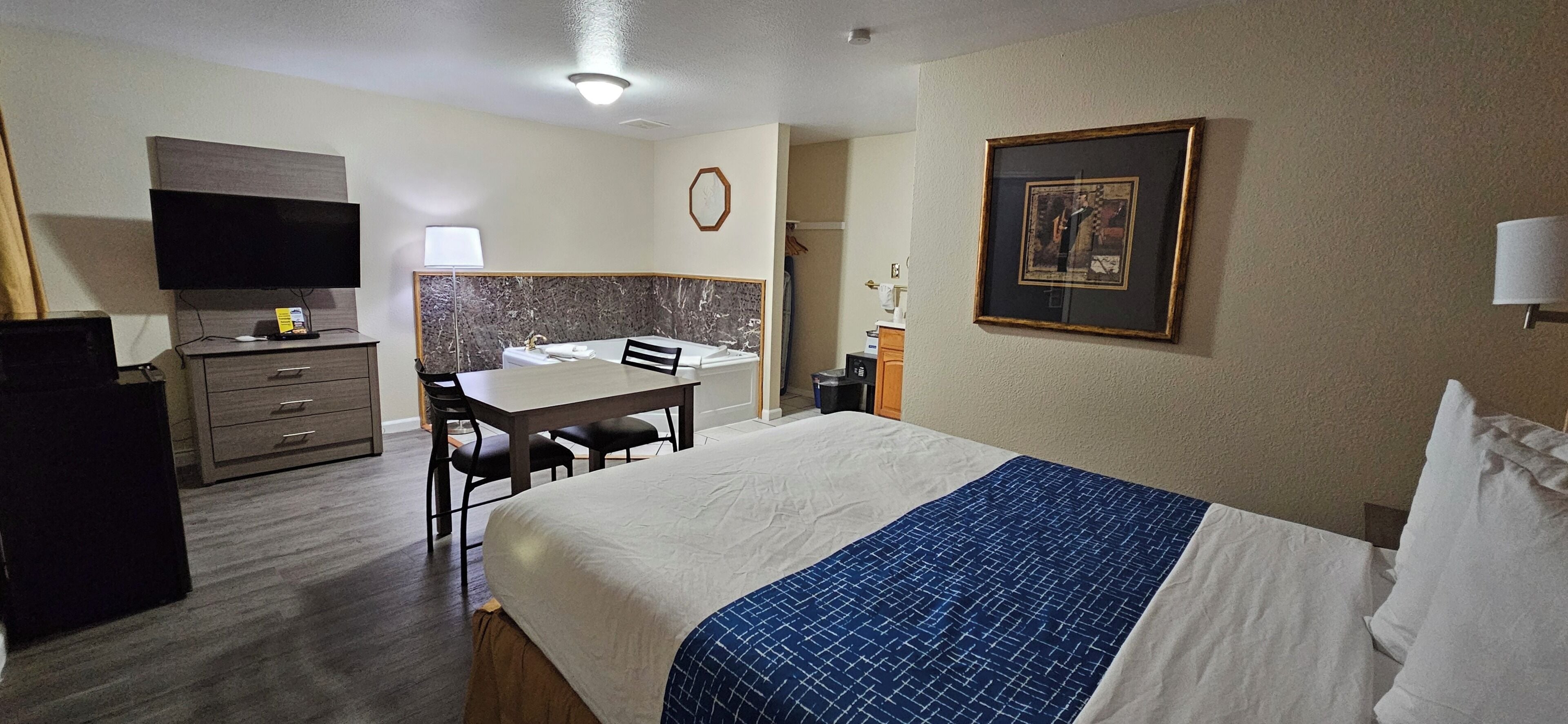 A hotel room with a bed, a desk, a chair, a television, a lamp, and a framed picture on the wall.