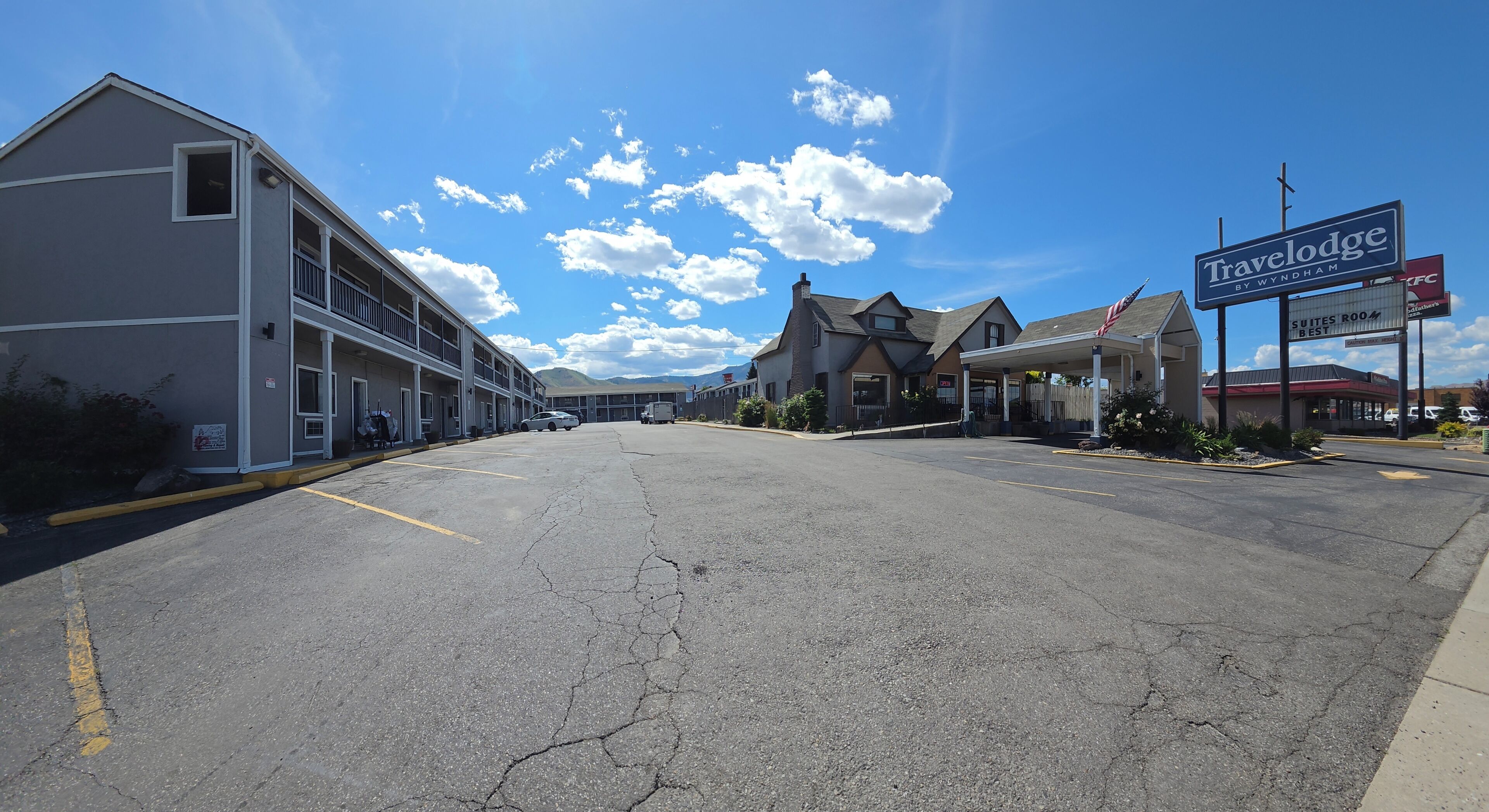 A Travelodge by Wyndham with a Suites Room, a parking lot, and a building with a balcony on the left.