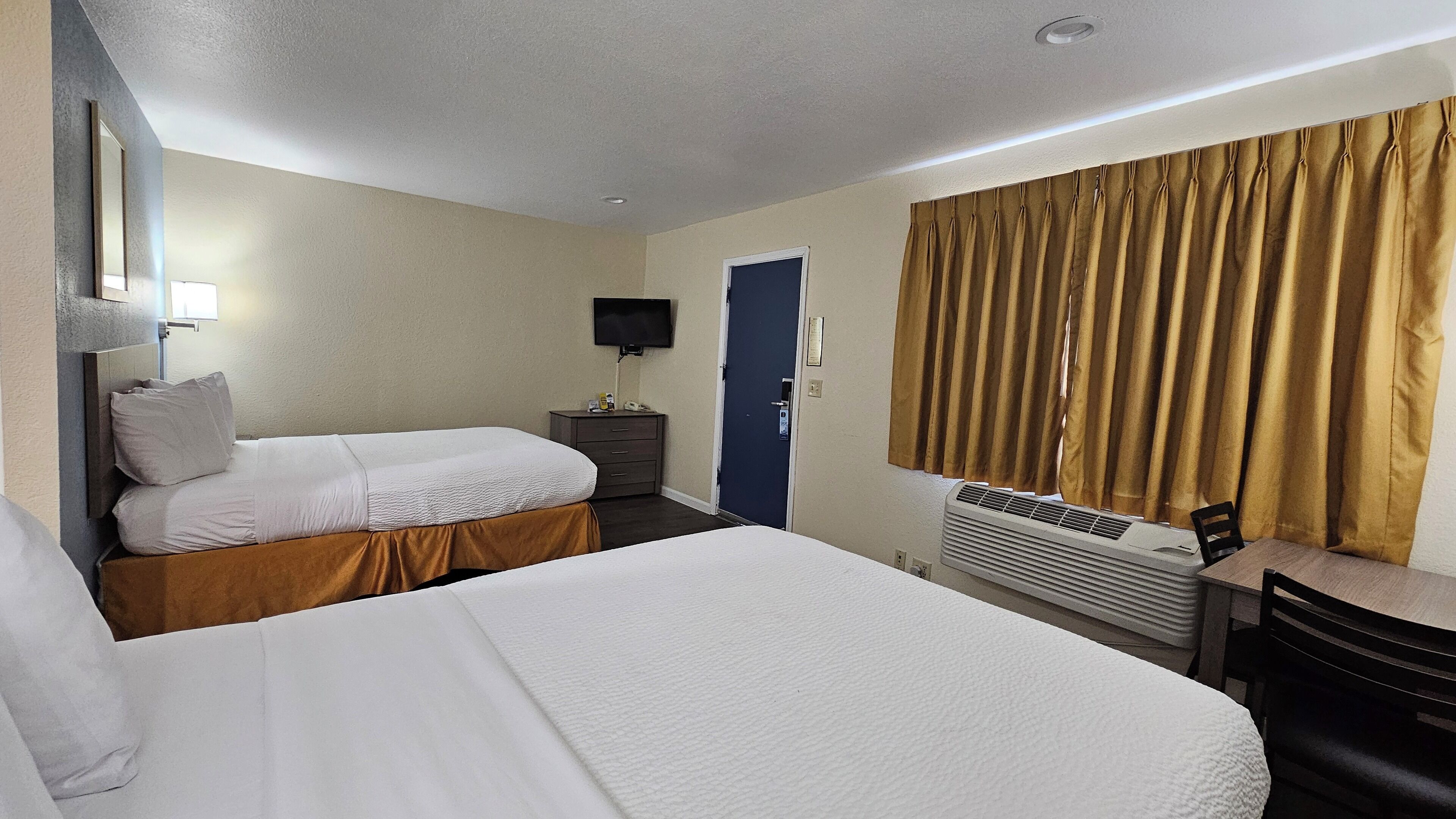 Habitación de hotel con dos camas, un escritorio, una silla, un televisor y una ventana con cortinas.