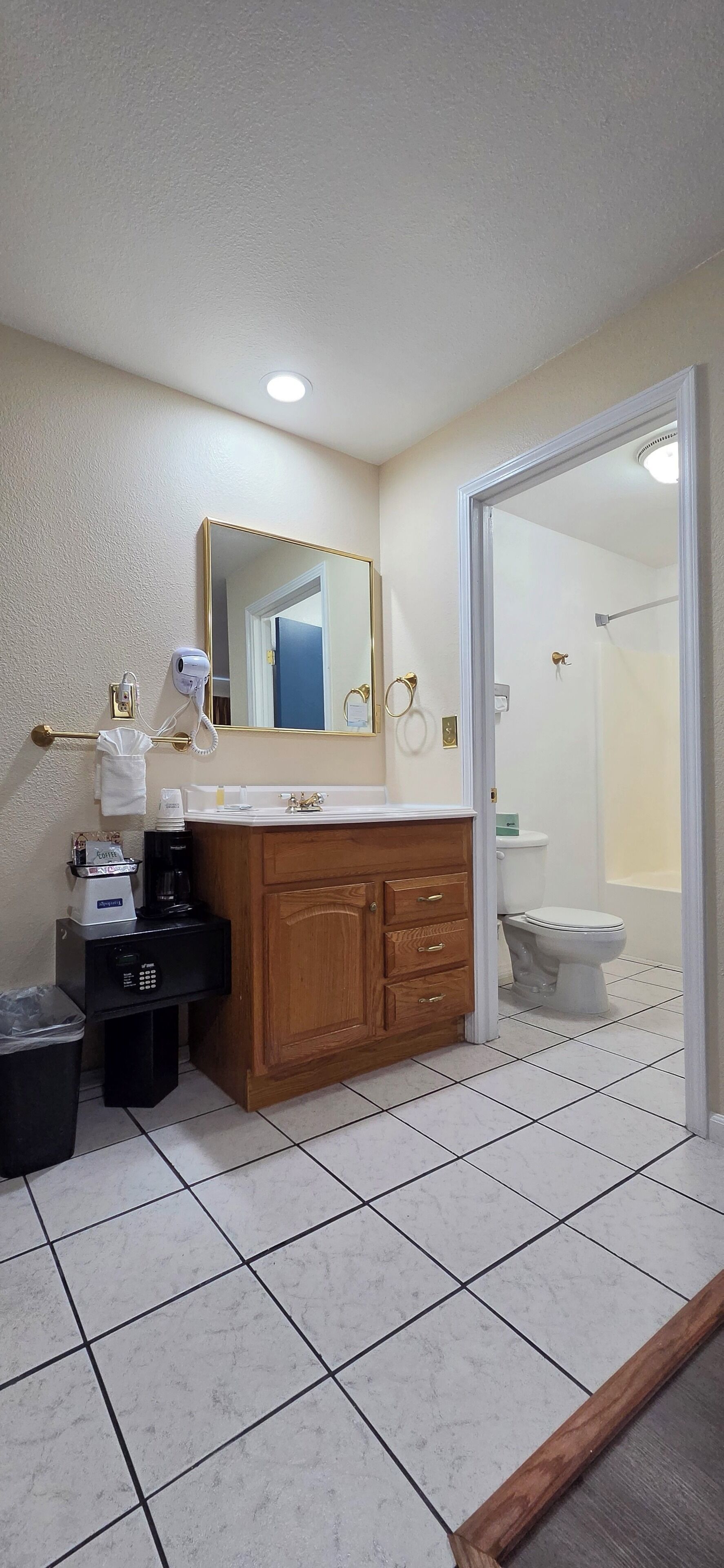 Une salle de bain avec un meuble-lavabo en bois, un miroir, un sèche-cheveux, une machine à café et des toilettes.