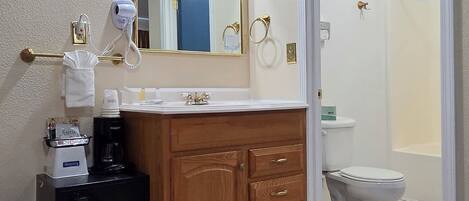 Une salle de bain avec un meuble-lavabo en bois, un miroir, un sèche-cheveux, une machine à café et des toilettes.
