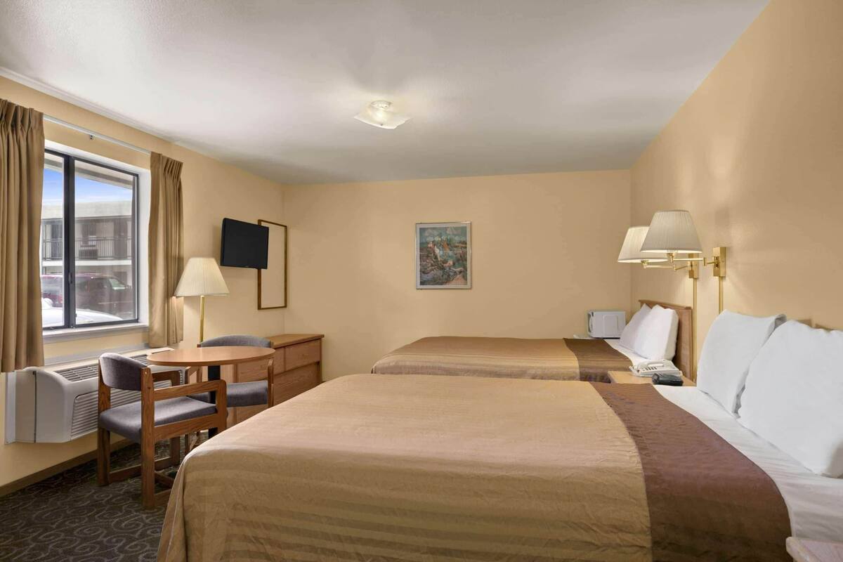 A hotel room with two beds, a desk, a chair, a TV, and a painting on the wall.