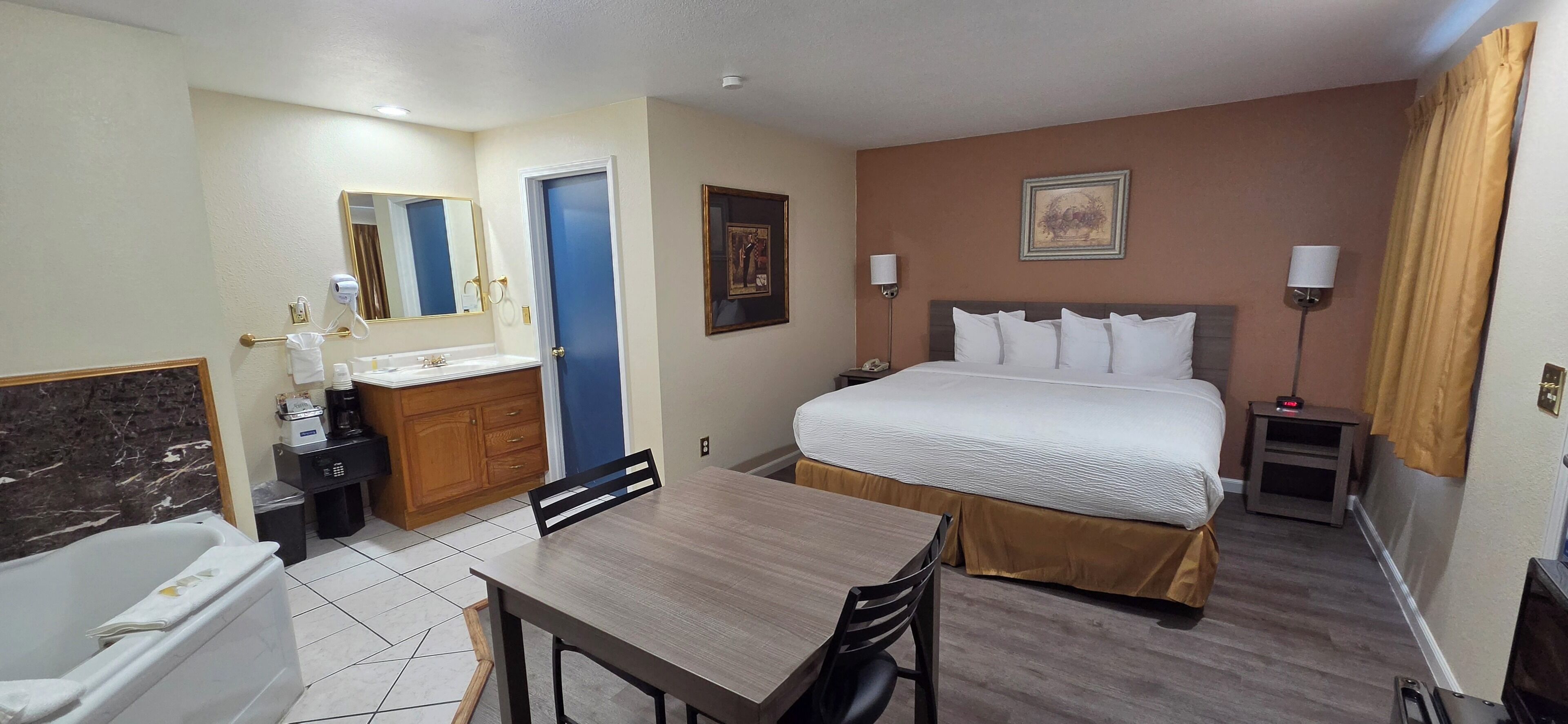 Habitación de hotel con cama, escritorio, silla, baño con bañera, lavamanos y espejo.