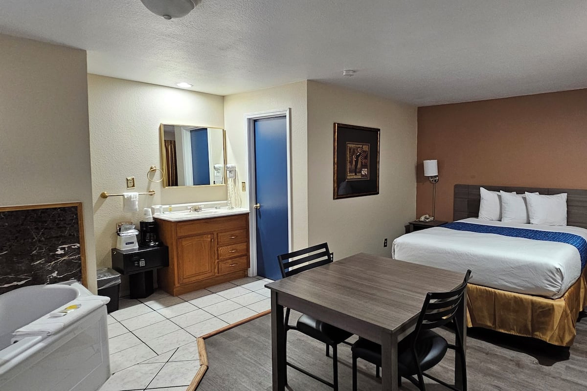 A hotel room with a bed, a desk, a chair, a bathroom with a bathtub, a vanity, and a nightstand.