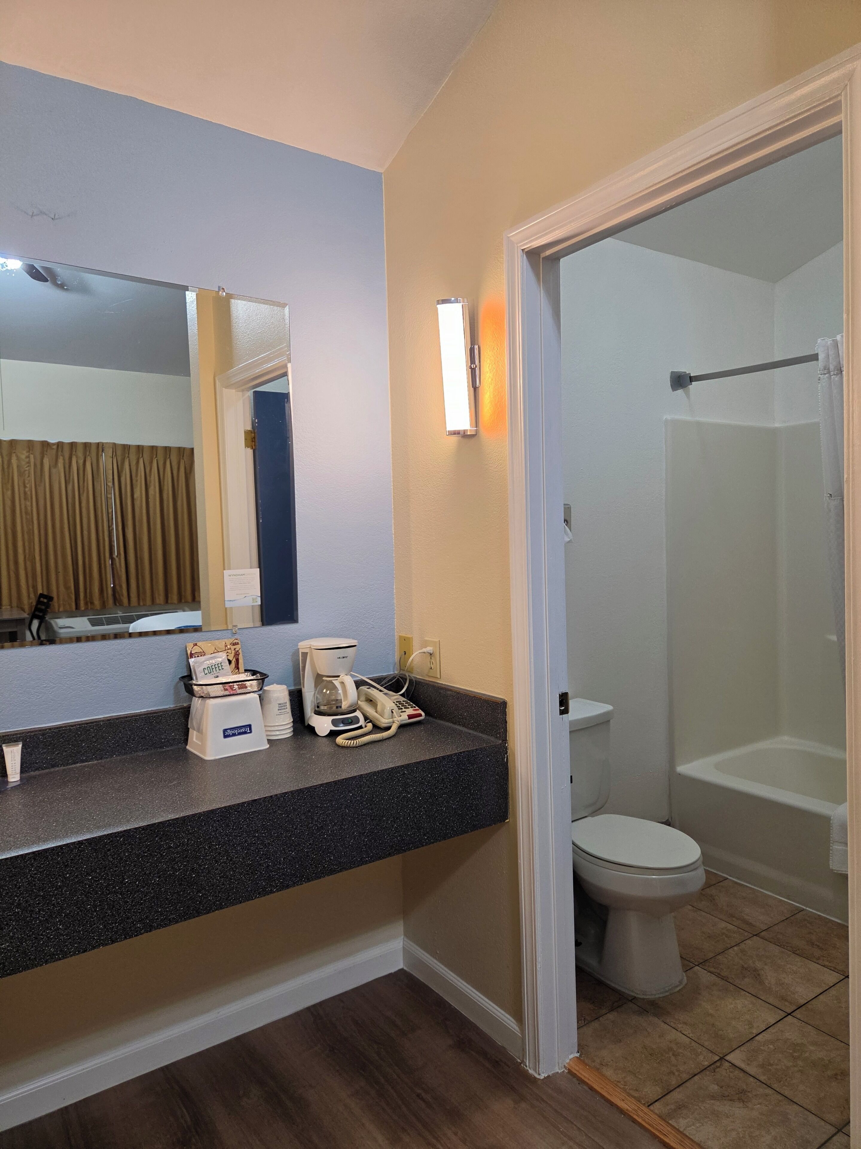 Ein Hotelbad mit Toilette, Dusche und einem Waschtisch mit Kaffeemaschine und Telefon.