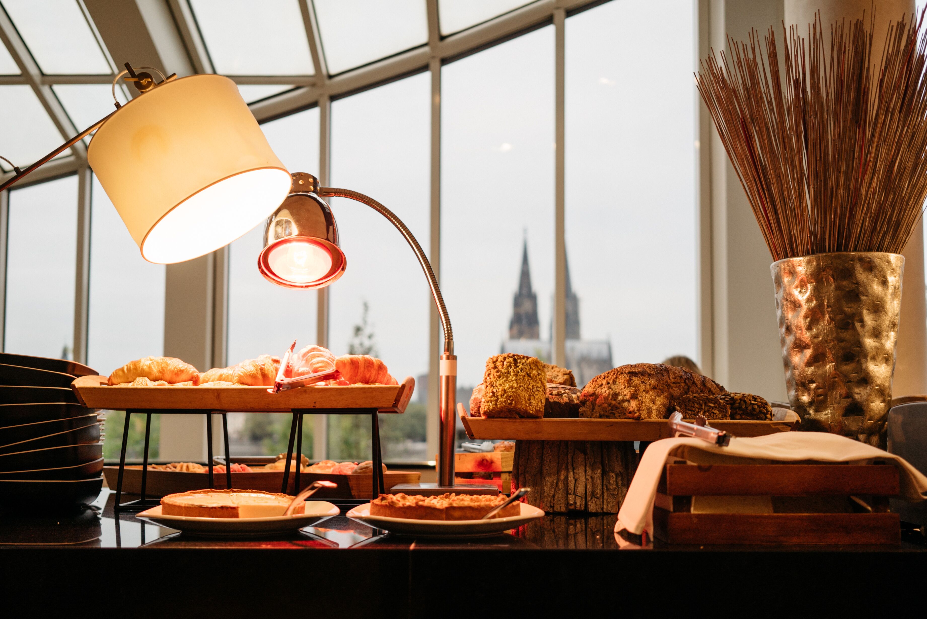 A breakfast buffet with various pastries and a view of a city skyline through large windows.