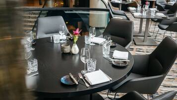 A round dining table set with plates, cutlery, and glasses, surrounded by black chairs in a modern interior.