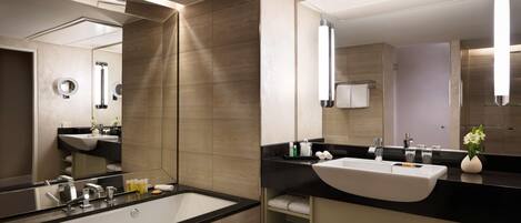 Un baño moderno con una bañera grande, un lavabo y un espejo. Hay repisas con toallas y artículos de aseo.