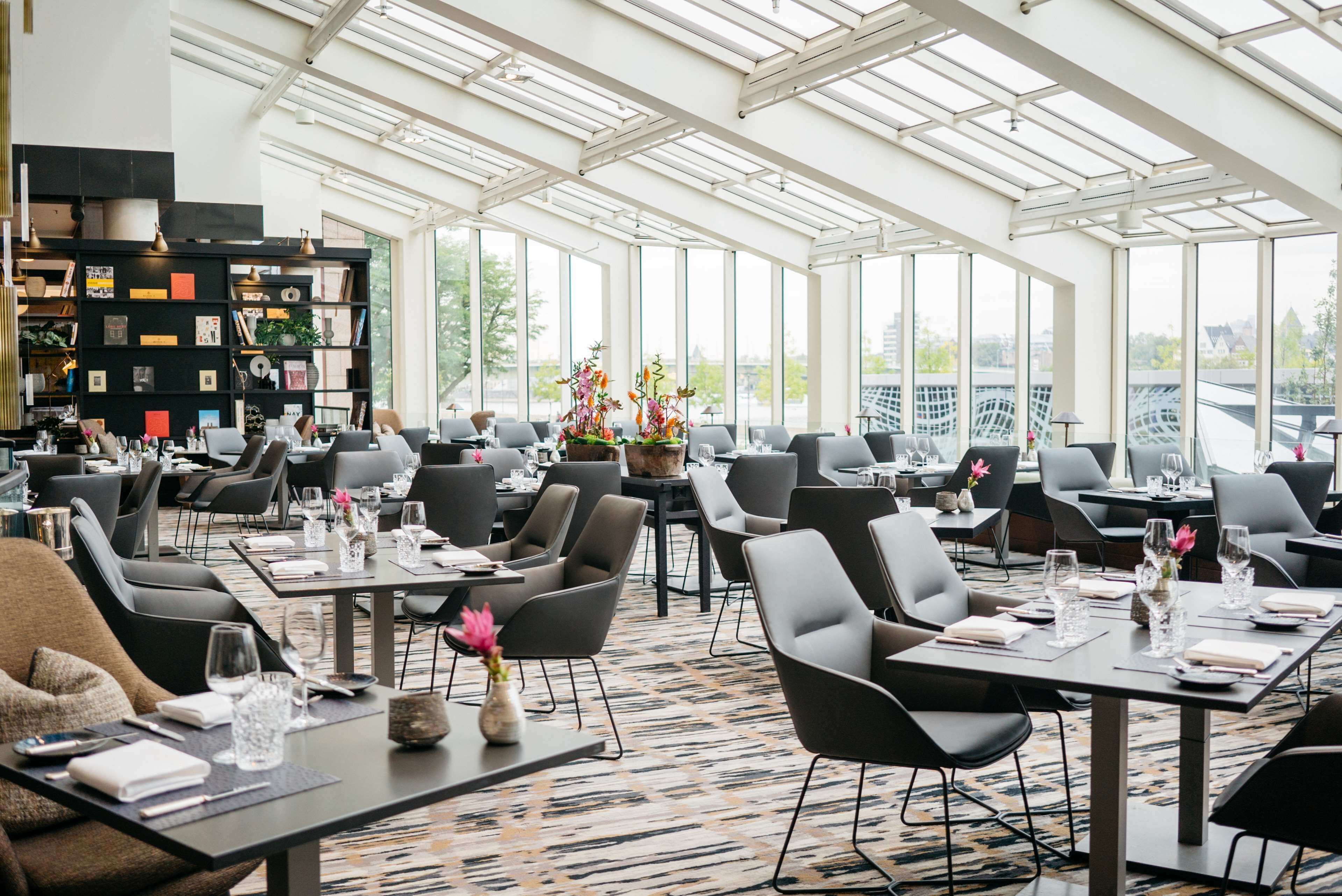 Un restaurante amplio con techos altos y ventanas grandes, con muebles modernos y un arreglo floral central.