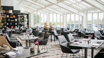 Un restaurante amplio con techos altos y ventanas grandes, con muebles modernos y un arreglo floral central.