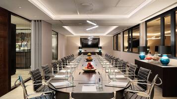 A modern conference room with a long table, chairs, and a central fruit bowl.