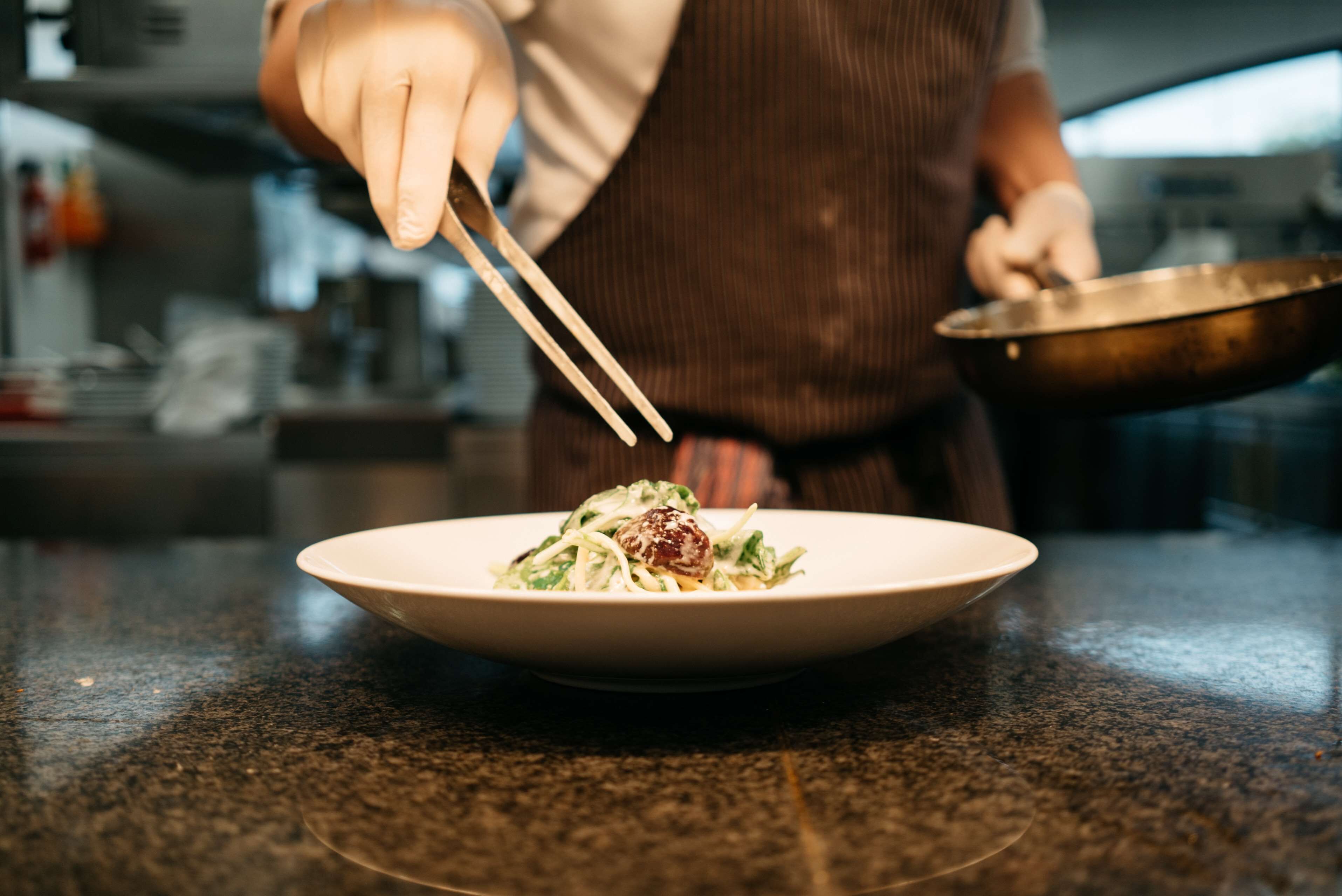 A person holding a bowl with chopsticks over a plate of food.