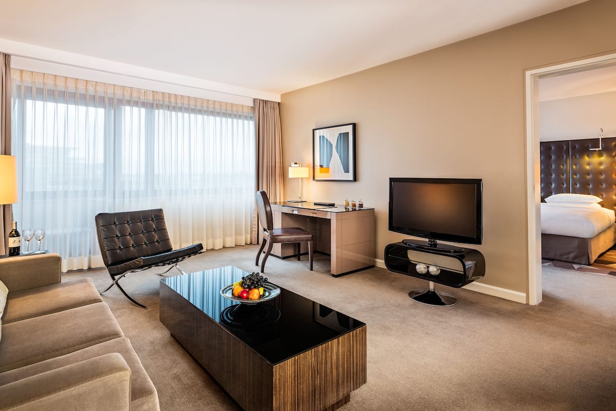 A hotel room with a sofa, a coffee table with fruit, a TV, a desk, and a bed.
